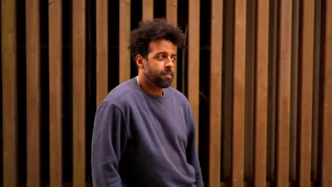 A man in a blue sweatshirt is dancing in front of a wooden fence Stock Footage 277645661