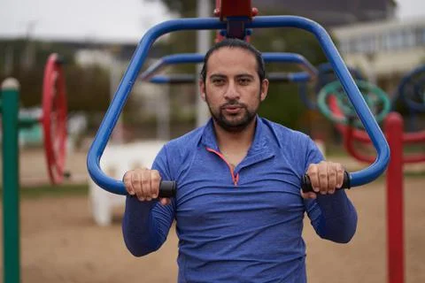 Man in blue t-shirt performs body weight exercises in public park. Stock Photos