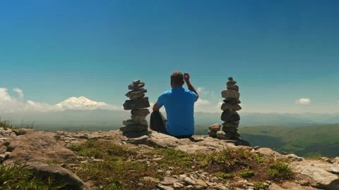 Man in blue t shirt is sitting between two balance pyramids and throwing small Stock Footage 151251953