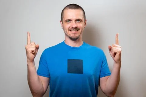 Man in blue tshirt looking in camera and pointing up by fingers Stock Photos