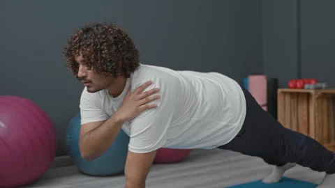 Man on blue yoga mat in studio doing plank with shoulder tap beside pink ex.. Stock Footage 337406784