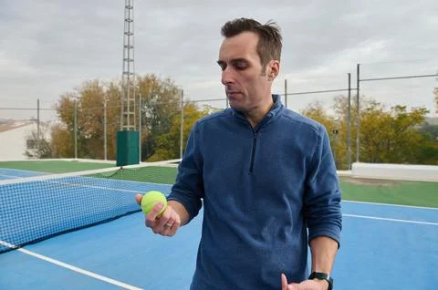 Man In Blue Zip-Neck Pullover On Bright Blue Tennis Court Preparing To Serve Stock Photos