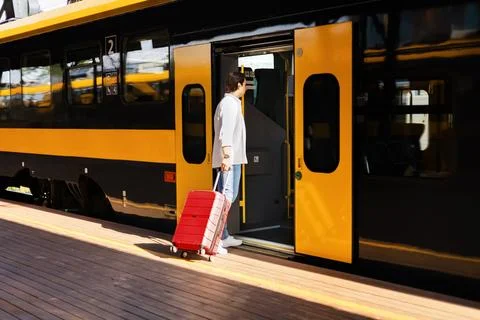 Man boarding a train on a railway platform with a suitcase, illustrating ec.. Stock-Fotos