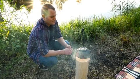 Man boiling a kettle on a fire outdoor Stock Footage 81768089