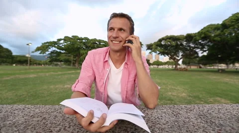 Man With Book Talking On Phone In The Park Stock Footage 55630336