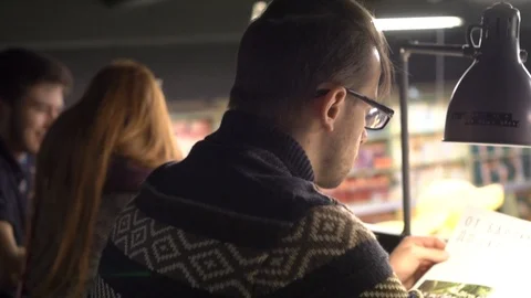 A man in a bookstore sits at a table and leafs through a magazine in the light o 動画素材 101721233