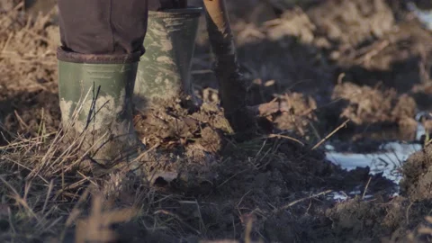 A man in boots full of mud digs with a shovel in the mud Vídeos de archivo 165428816