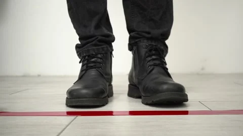 Man in boots standing behind the red tape floor marking for social distance Stockbeeldmateriaal 147138589