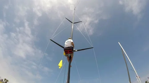 Man in boseman chair cleaning the rigging of racing yacht blue sky and noon  Stock Footage 67521554