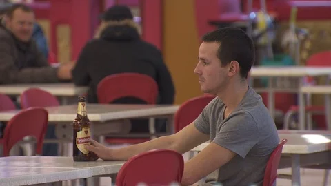 A man with a bottle of beer sits at a table in a mall. Stock Footage 113797987