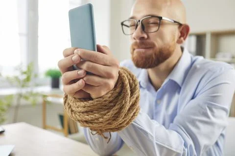 Man With Bound Hands Using Smartphone Reflecting Digital Addiction Stock Photos