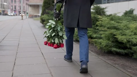 Man with bouquet red roses quickly goes meeting Against background green bushes Stock Footage 230257622