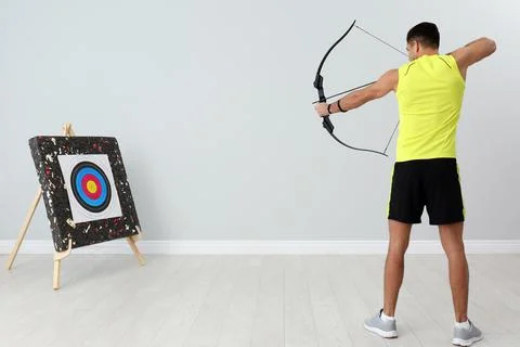 Man with bow and arrow aiming at archery target indoors Фото