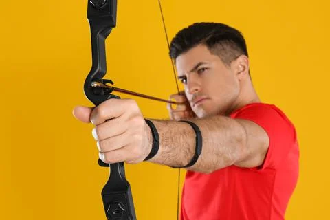 Man with bow and arrow practicing archery against yellow background, focus on Stock Photos