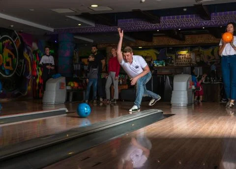 A man in a bowling alley throws a blue european ball in jeans and a white T Stock Photos