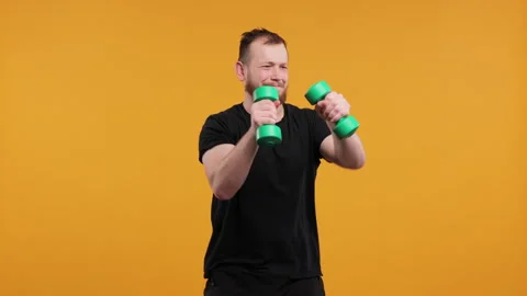 Man Boxing Playfully with Light Green Dumbbells on a Yellow Background Stock Footage 275926628
