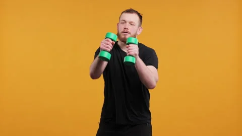 Man Boxing Playfully with Light Green Dumbbells on a Yellow Background Stock Footage 275948184