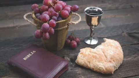 Man breaking the bread, with wine, grapes and Bible in the background Video stock 105683347