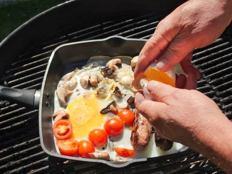 Man breaking an egg cooking fresh sausage eggs tomatoes and mushrooms break.. Stock Photos