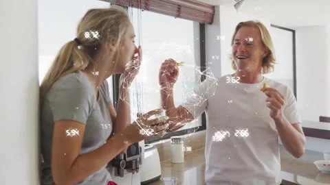 Man breaking pastry and feeding woman in data-driven breakfast in kitchen while Stock Footage 313570456