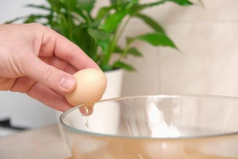 A man breaks a chicken egg on the edge of transparent glass bowl. The process of 스톡 사진