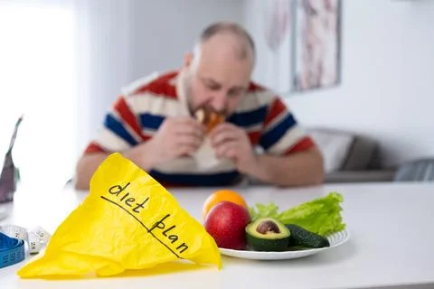 Man Breaks Diet, Eats Junk Food Despite Healthy Food Nearby Stock Photos