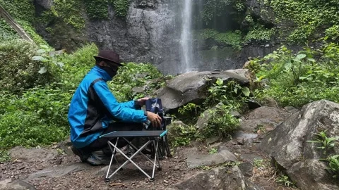 Man Brewing Coffee Next to Waterfall, Green Forest Environment, Static Shot Stock Footage 324850266