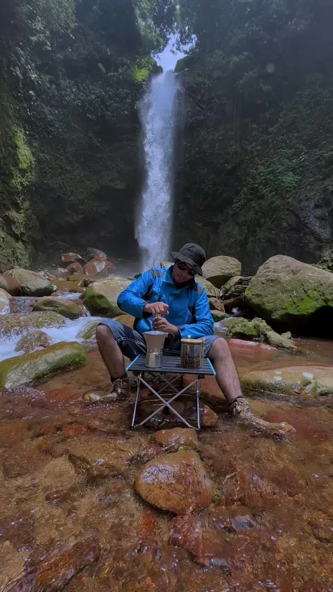 Man Brewing Pour Over Coffee in Jungle Stream by Waterfall Vertical Stock Footage 321104750