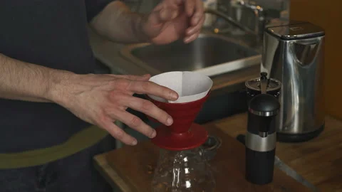 A man brews ground coffee through a paper filter in the kitchen in the morning Stock Footage 171155205