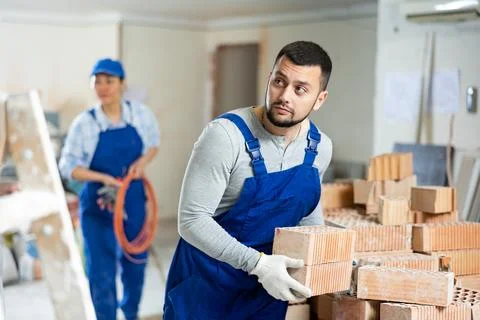 Man bricklayer carrying bricks during repair works in apartment Stock Photos