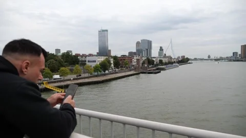 Man on bridge checking phone with city skyline and river in background Stock Footage 319407187