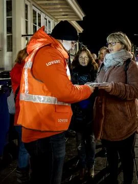 Man in bright orange jacket checks tickets from queuing passengers Stock Photos