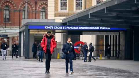 A man in a bright red coat walks next to a woman across King's Cross Square o Stock Footage 127383716