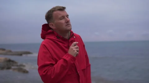 A man in a bright red jacket smokes an electronic cigarette in the evening by Stock Footage 274341834