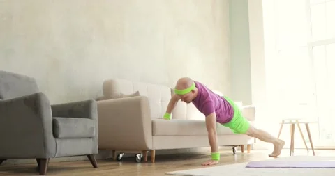 Man in bright sportswear is doing push-ups exercises using sofa at home. Vídeo Stock 131067829