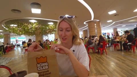 Man bringing burger king takeaway to his girlfriend in a food court Stock Footage 324718364