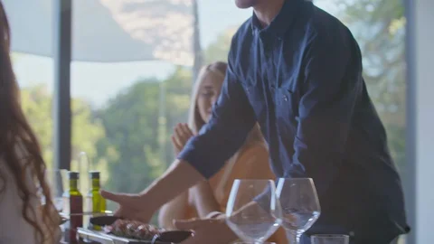 Man bringing grilled meat to lunch table. Group of happy friends talking 스톡 동영상 128985102