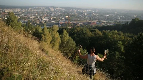 Man with broad shoulders stands on a mountain and looks at the city. muscular Video stock 126496018