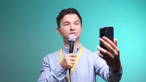 Man broadcasting live, holding a smartphone for a selfie video and a microphone Stock Footage 342774596