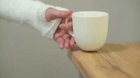A man with a broken arm in a plaster cast takes and puts a mug of the table Stock Footage 234134683
