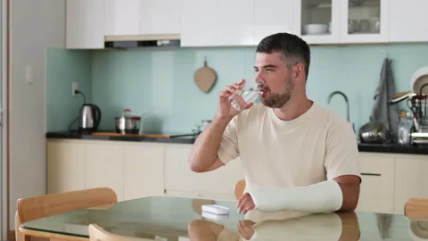 Man with broken arm takes medication in cozy kitchen. Stock Footage 290842206