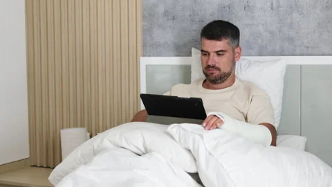 Man with broken arm using tablet in bed while. Video stock 290844239