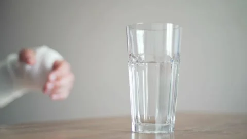 A man with a broken bone tries to take a glass of water. Disability. Bandage on Vídeos de archivo 133078025