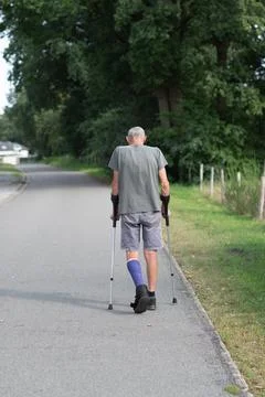 A man with a broken leg is walking down the street, on his left leg he has a Stock Photos