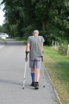 A man with a broken leg is walking down the street, on his left leg he has a Stock Photos