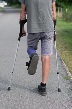 A man with a broken leg is walking down the street, on his left leg he has .. Stock Photos