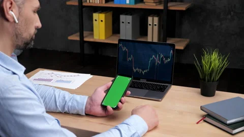 Man broker scrolling green screen smartphone, laptop with stock exchange chart Stock Footage 168727933