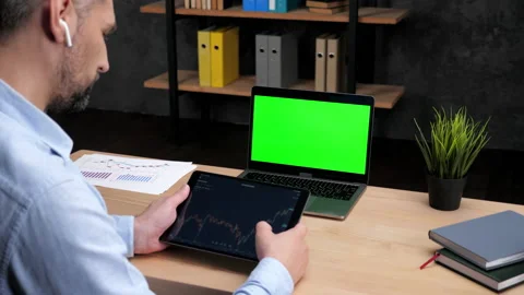 Man broker scrolling tablet with stock exchange chart, laptop with green screen Stock Footage 170130735