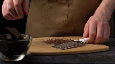 A man in a brown apron with a grater grinds chocolate 库存影片 100407480