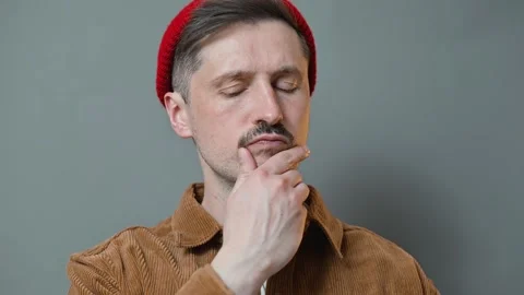 A man in a brown jacket and red beanie shows various thoughtful expressions Видео 337643279